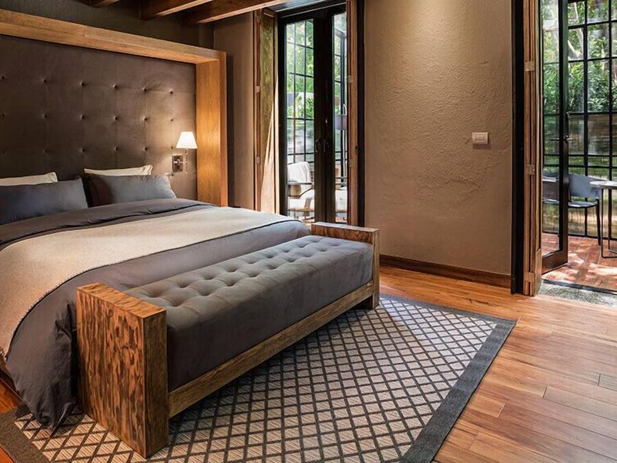 A modern bedroom with a large bed, wooden headboard, two bedside lamps, and a view of an outdoor patio.