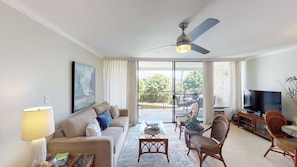 Relax in a spacious living area with a comfortable sofa, floor lamp, and flat-screen TV, opening to a balcony with a serene view.