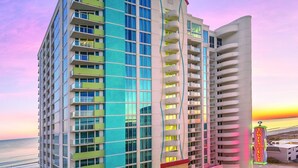 Un hotel de varios pisos con un diseño moderno, que cuenta con balcones, ventanas amplias y un área de piscina.