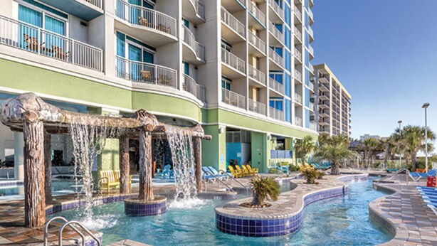 Zona de piscina hotelera con múltiples fuentes de agua, incluyendo una fuente central y jacuzzis circundantes.