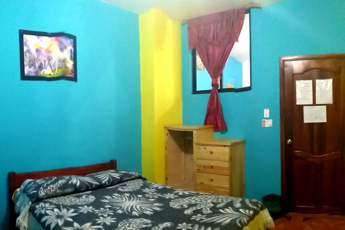 Quarto com cama, cómoda de madeira, guarda-roupa, quadro na parede e porta com aviso.