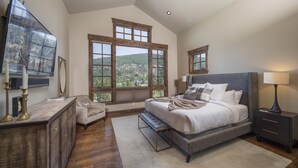 Une chambre dotée d’un grand lit, d’une table de chevet, d’une commode, d’un téléviseur et offrant une vue sur un paysage montagneux grâce à de grandes fenêtres.