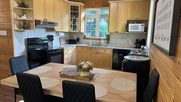 Une cuisine rustique aménagée dans une cabane en bois, avec une table à manger, des chaises et une vue sur l’extérieur.