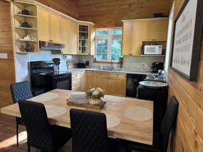 A wooden cabin kitchen with a dining table, chairs, and a view of the outdoors.