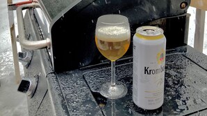 Une table avec un verre de bière et une canette de bière Krombacher, avec une vue sur un paysage enneigé.