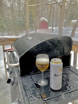 Una mesa con un vaso de cerveza y una lata de cerveza Krombacher, con vista al exterior nevado.