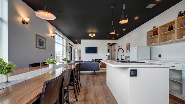 A modern kitchen with a central island, wooden flooring, pendant lighting, and built-in shelving. - Raven Inn Whitehorse (Whitehorse)