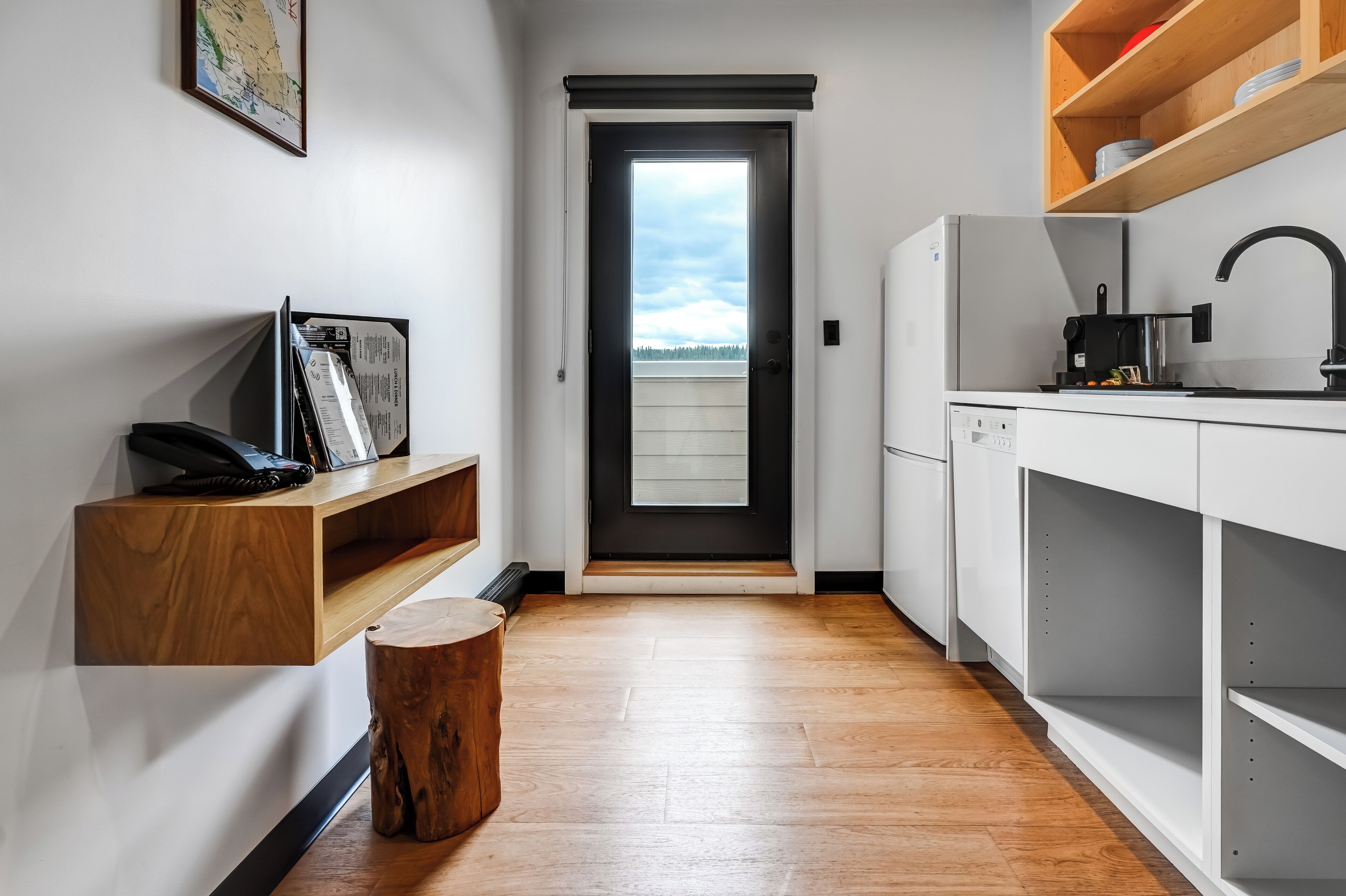 A modern kitchen with a black and white color scheme, a wooden floor, and a view through a door to the outside.