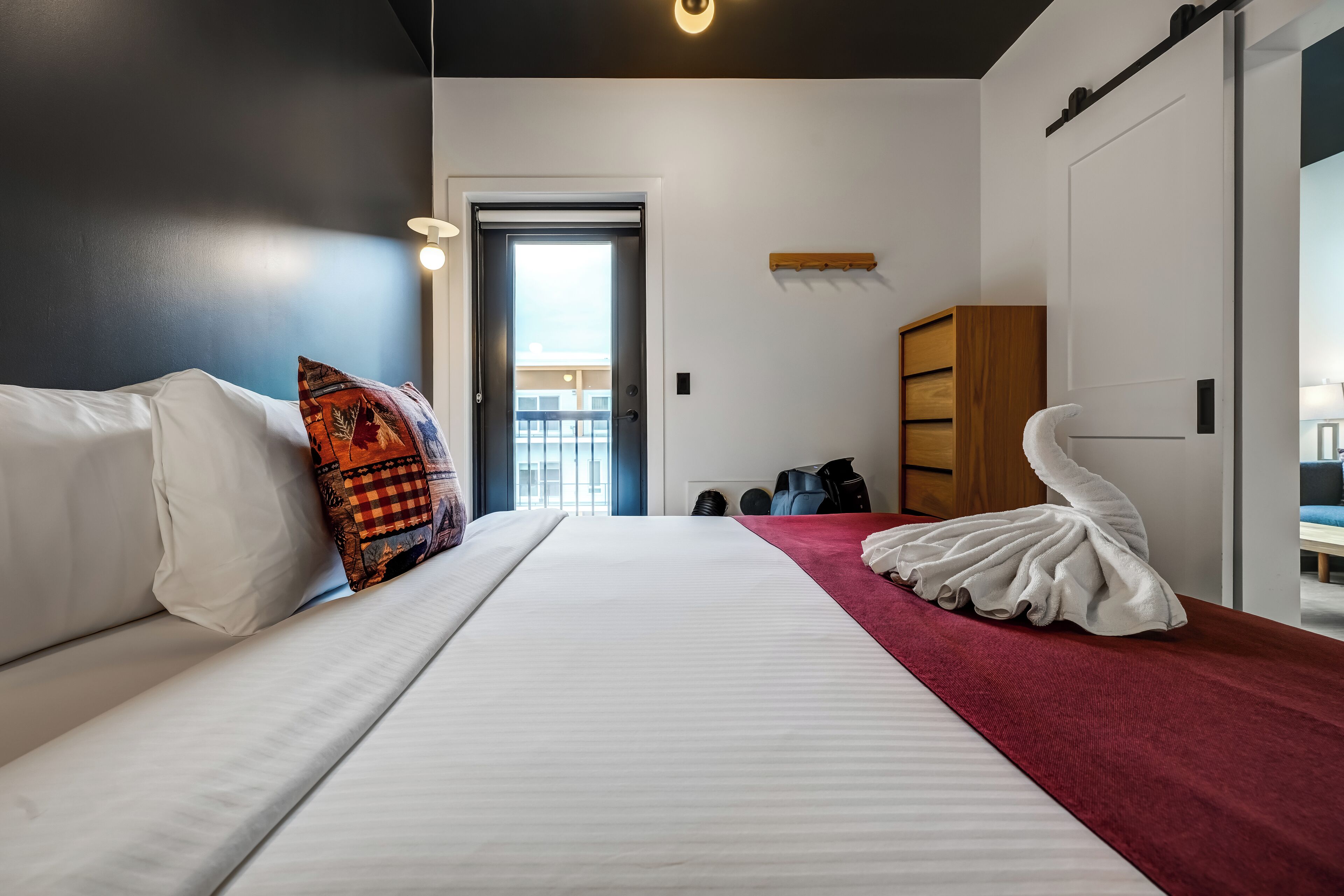 Moderni hotellihuone, jossa on suuri sänky, punainen tehosteseinä, valkoinen tuoli ja ainutlaatuinen valkoinen veistos.