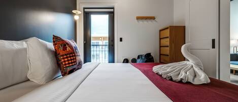 Een moderne hotelkamer met een groot bed, een rode accentmuur, een witte stoel en een unieke witte sculptuur.