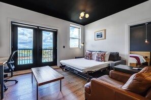 Ein modernes Zimmer mit Bett, Schreibtisch, Ledersofa und Blick ins Freie.