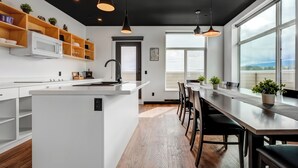 A modern kitchen with a central island, wooden shelves, and pendant lighting. - Raven Inn Whitehorse (Whitehorse)