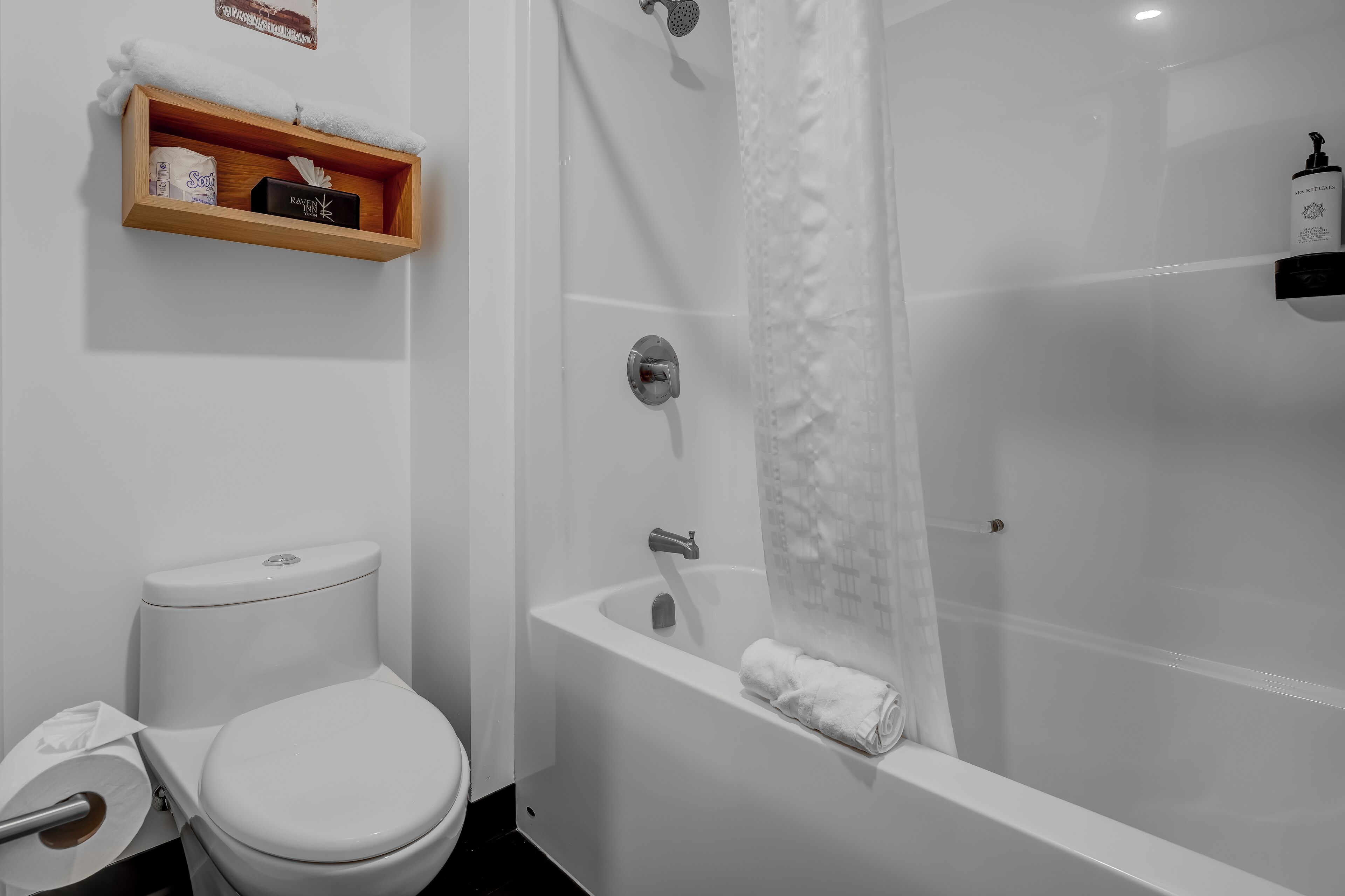 A modern bathroom with a toilet, a shower, and a wooden shelf with toiletries.