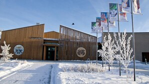 A building with a wooden facade, a circular emblem, and several flags. - Raven Inn Whitehorse (Whitehorse)