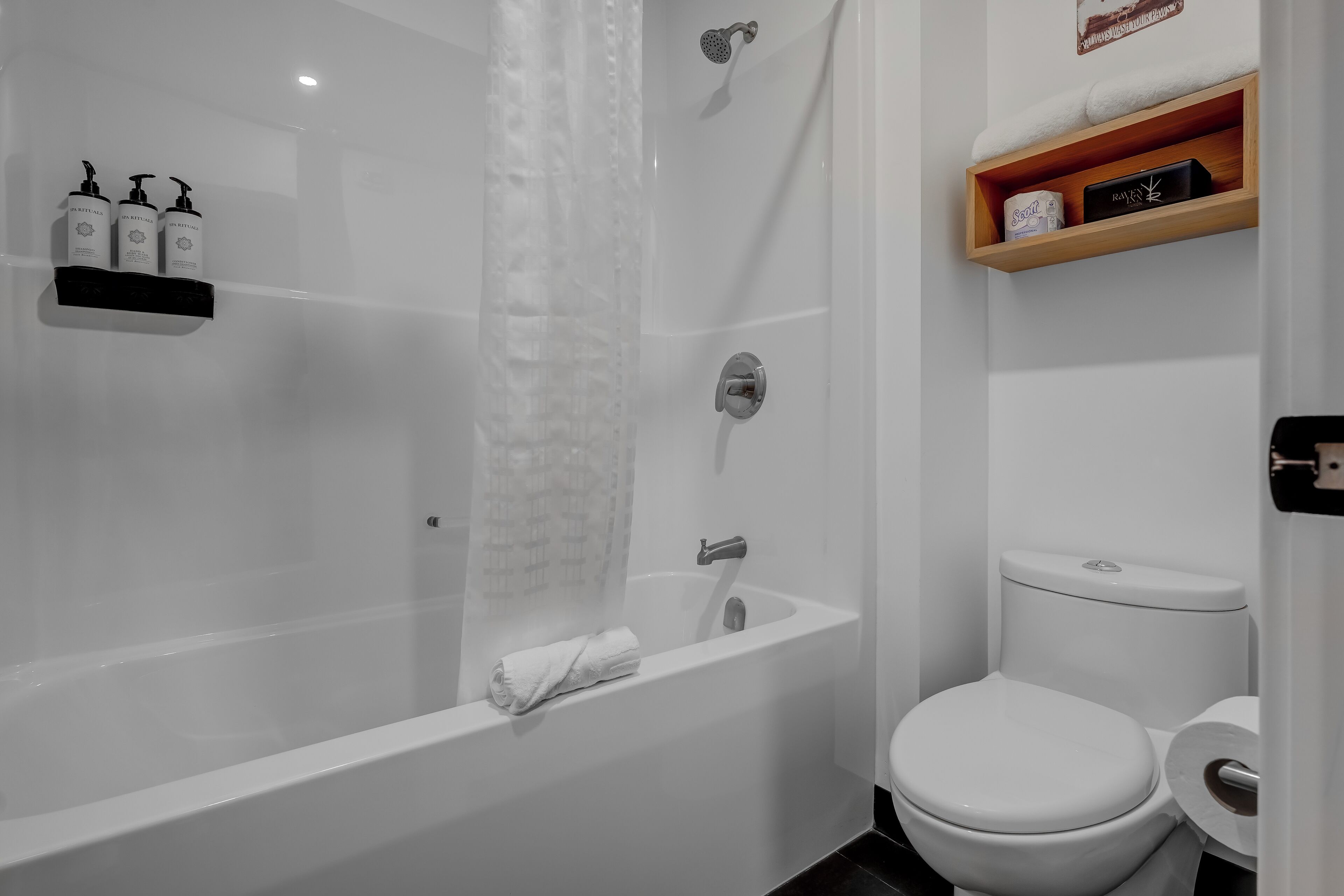 A modern bathroom with a bathtub, toilet, and a shelf with toiletries.