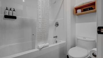 A modern bathroom with a bathtub, toilet, and a shelf with toiletries.