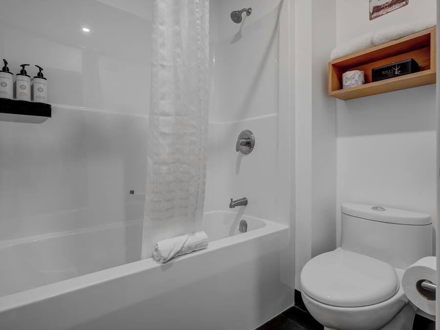 A modern bathroom with a bathtub, toilet, and a shelf with toiletries.