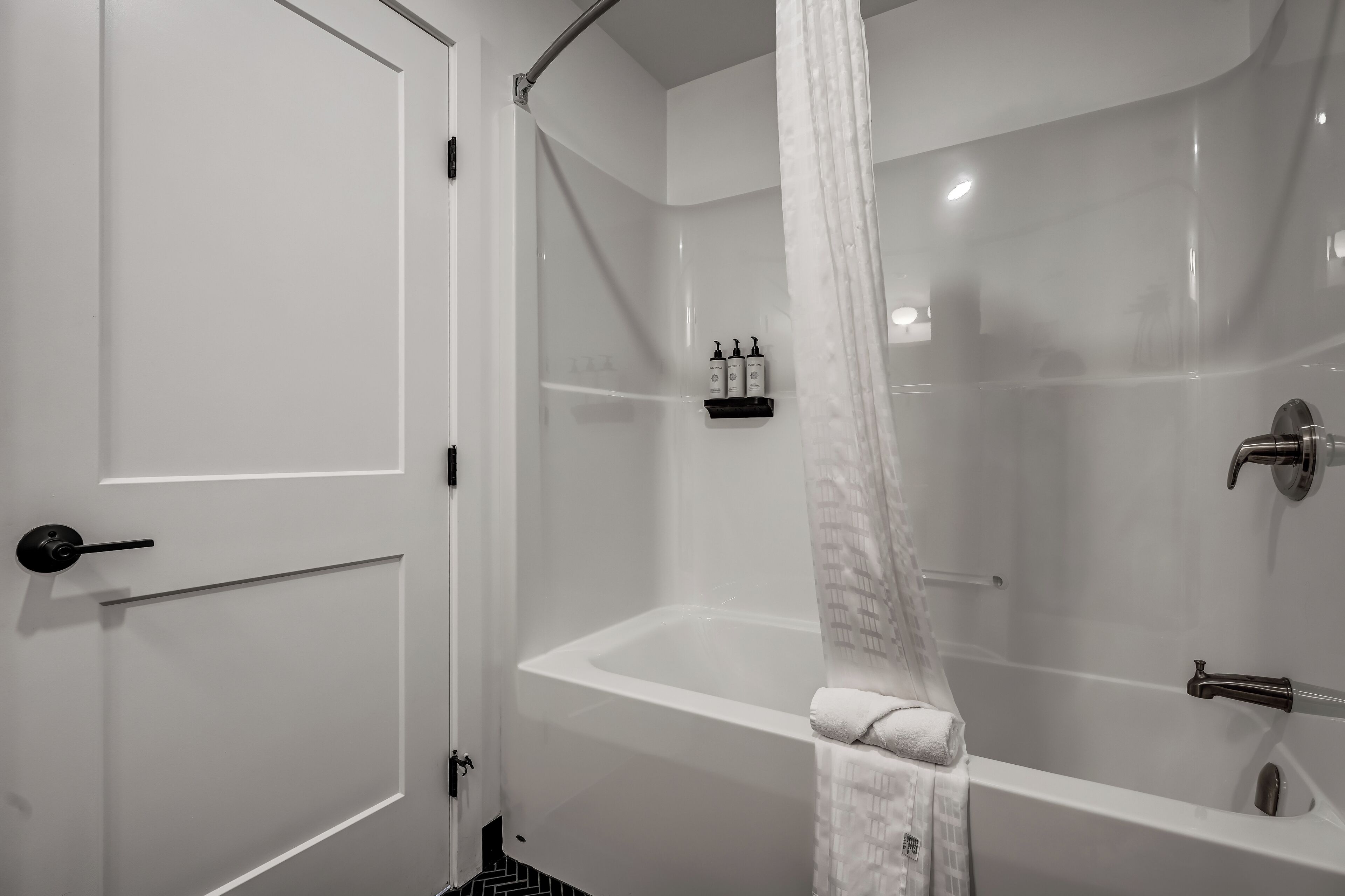 A modern bathroom with a bathtub, a shower area, and a door with a towel hanging on it.