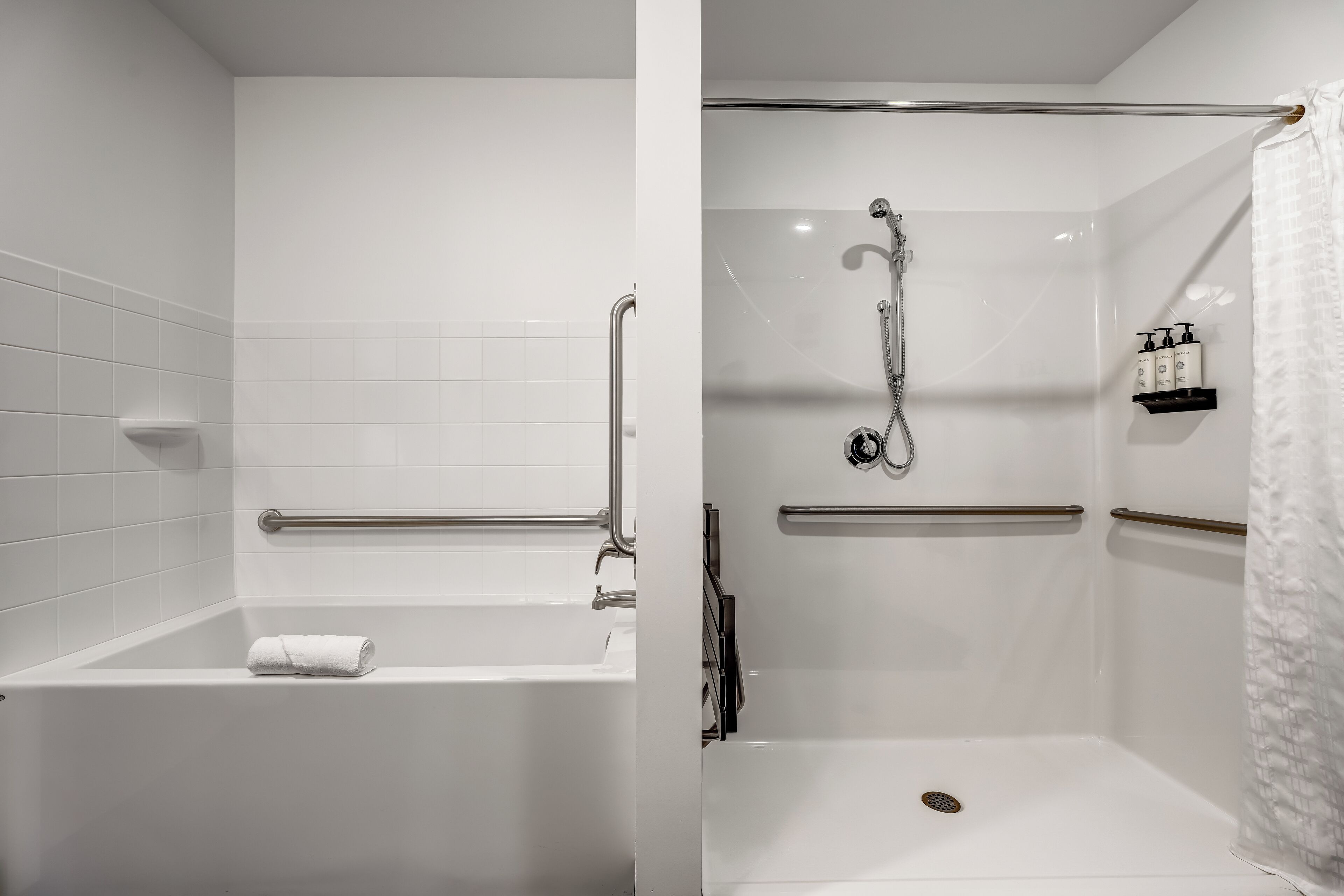 Een moderne badkamer met een bad, douche en handgrepen.