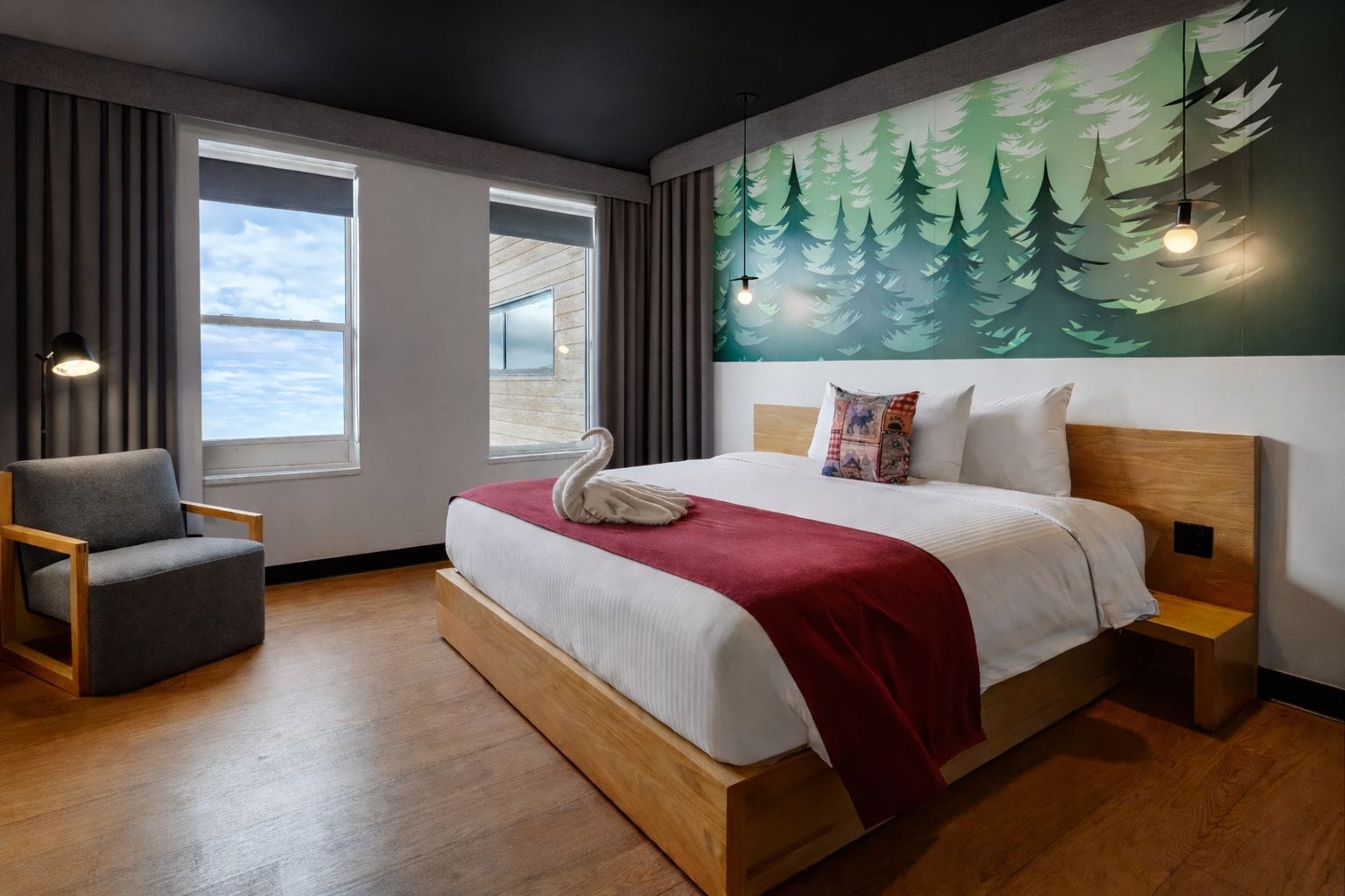 A modern hotel room with a large bed, a chair, a view of the sea, and a forest-themed wall mural.