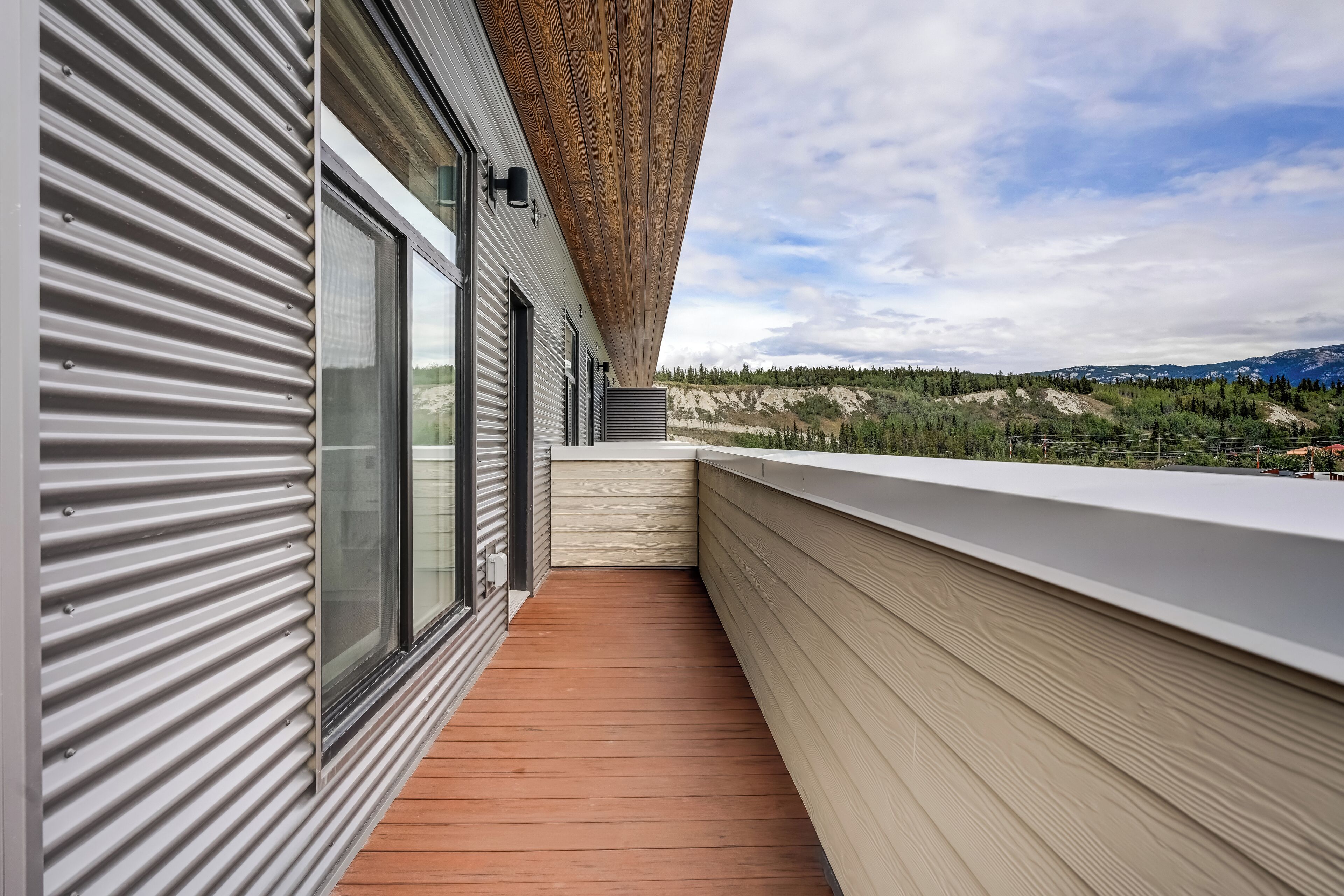 Un balcon moderne doté d’un plafond en lambris de bois, de grandes fenêtres et offrant une vue sur un paysage montagneux.
