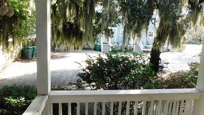 A porch with a view of a yard, including a tree with hanging moss, a white fence, and a golf cart.