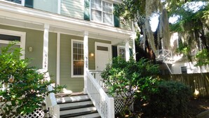 A two-story house with a front porch, a staircase leading to the entrance, and a wooden fence.