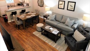 A modern living room with a grey sofa, black armchairs, and a wooden dining table with placemats.