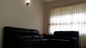 A living room with a black sectional sofa, a small table, and a window with sheer curtains. - Hotel Lans (Kandy)