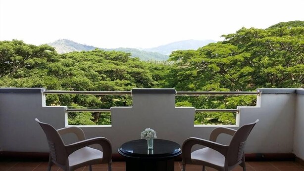 A balcony with two chairs and a table, overlooking a lush green landscape with trees and distant hills. - Hotel Lans (Kandy)