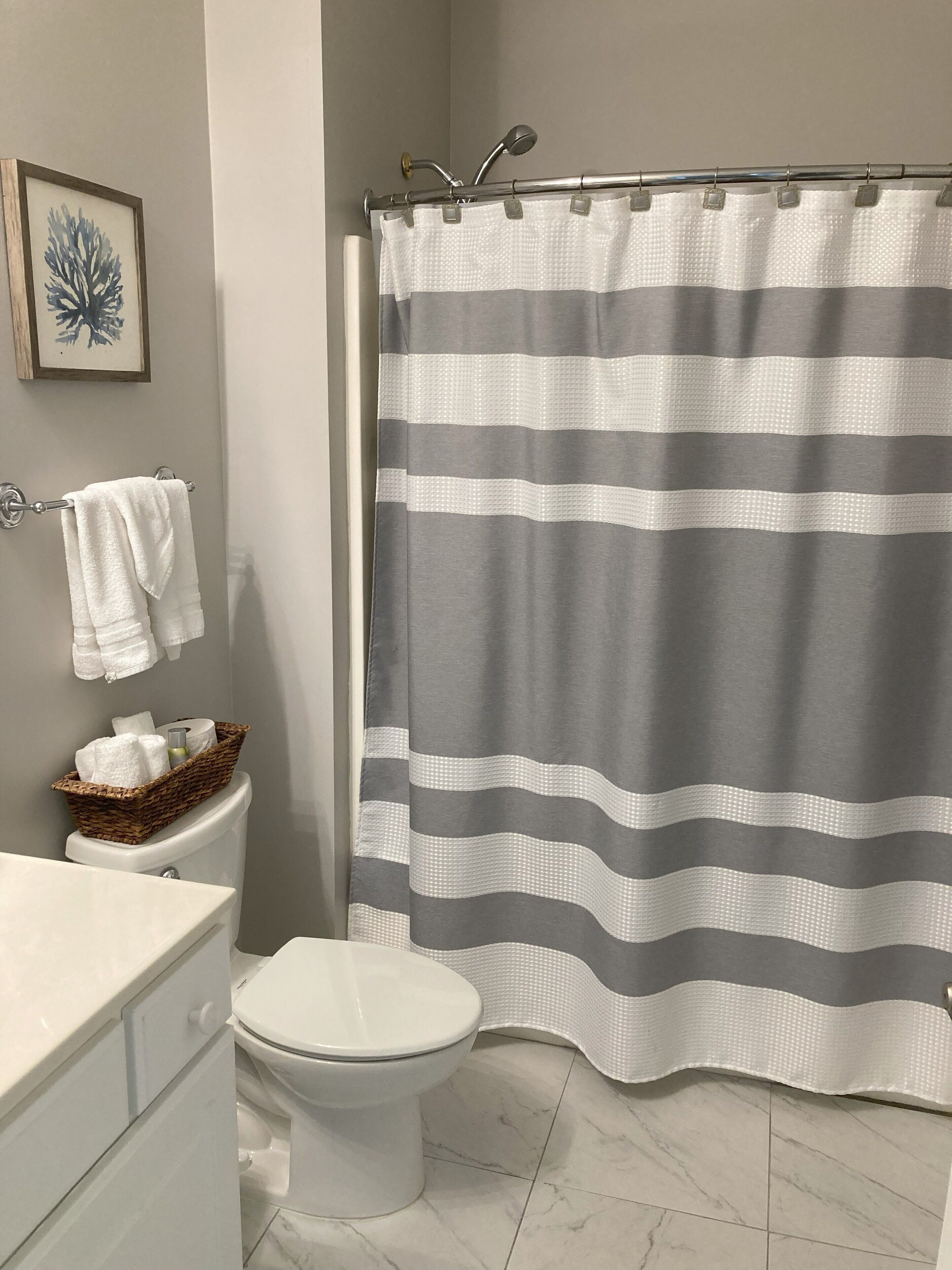 A bathroom with a toilet, a white sink, a basket of toiletries, and a shower curtain with horizontal stripes.
