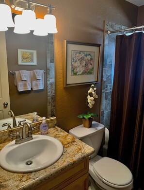A bathroom with a marble sink, a toilet, a framed floral painting, and a shower curtain.