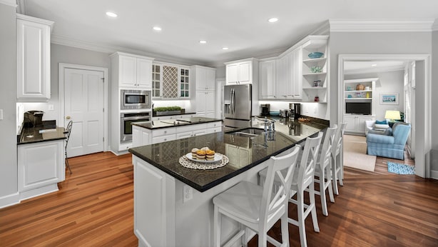 Una cocina moderna con armarios blancos, una isla central con taburetes de bar, electrodomésticos de acero inoxidable y una barra desayunadora.