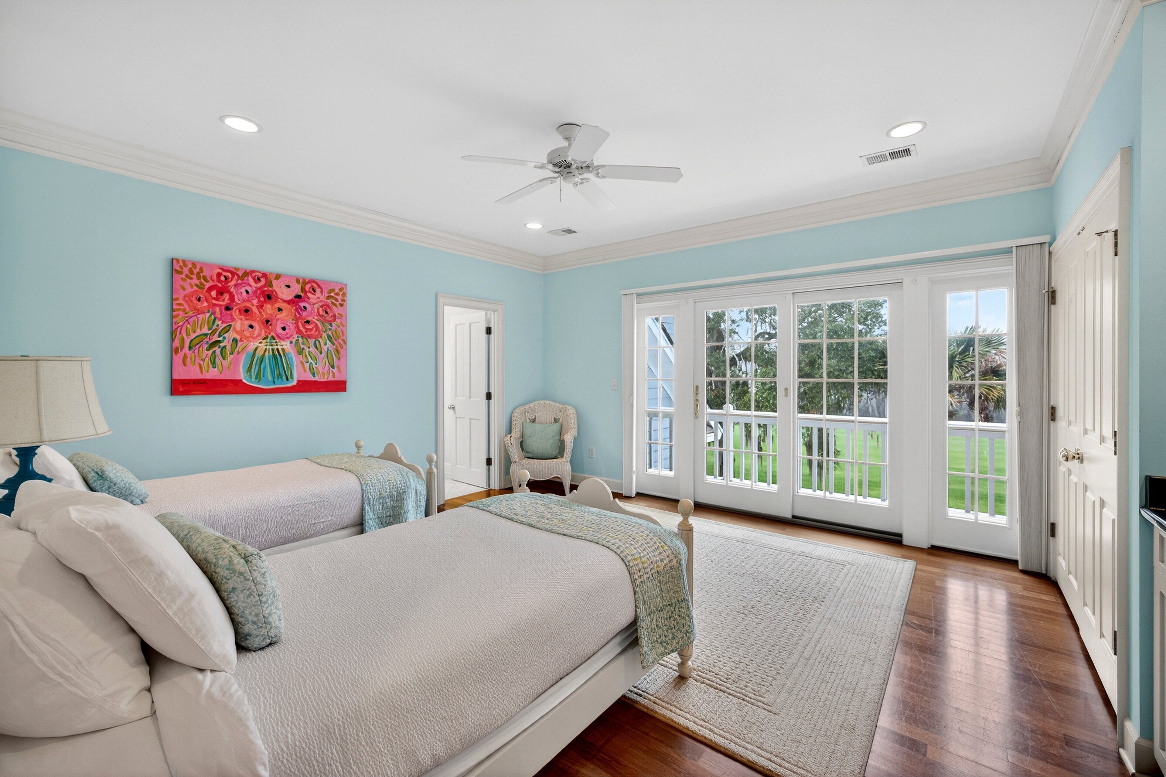 A bedroom with two beds, a ceiling fan, and a large window with a view of the outdoors.