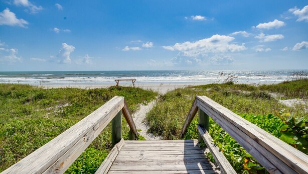 Une promenade en bois mène à une plage, et un banc en bois se trouve à son extrémité.
