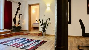 Ein modernes Interieur mit Holzboden, einem Streifenmuster-Teppich, einer hohen Pflanze und einer Tür zu einem anderen Raum.