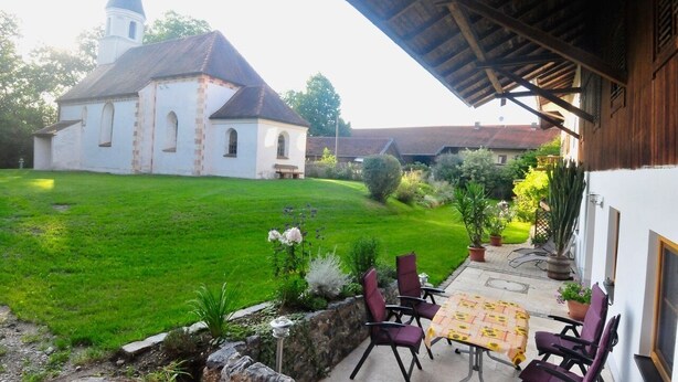 Eine überdachte Terrasse mit Gartenmöbeln, eine Rasenfläche und eine Kirche im Hintergrund.