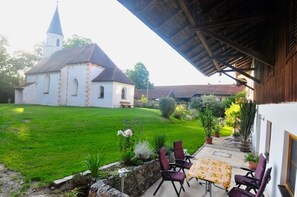 Um alpendre coberto com área de estar ao ar livre, gramado e uma igreja ao fundo.