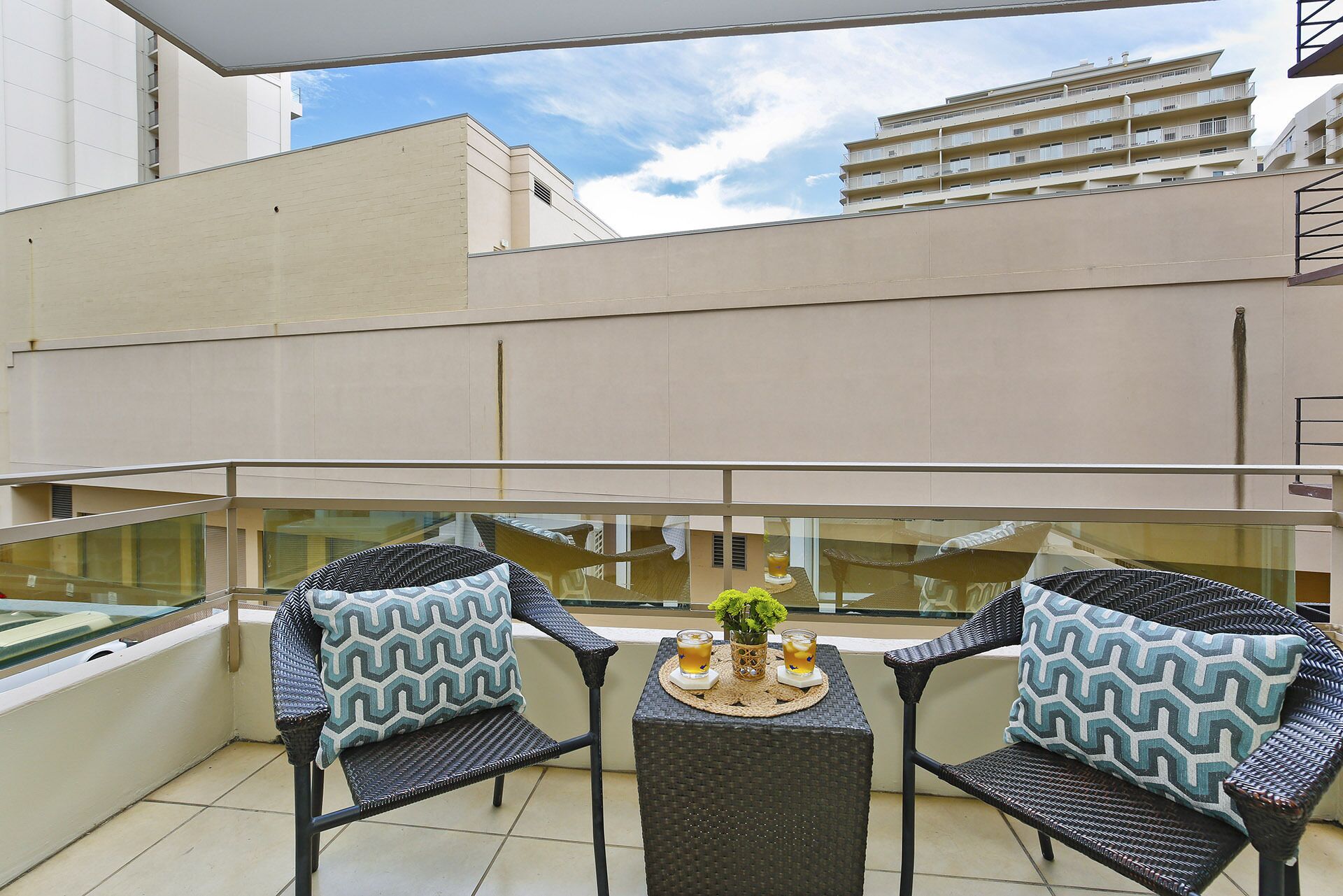 A balcony with two wicker chairs, a small table, and two glasses of drink.