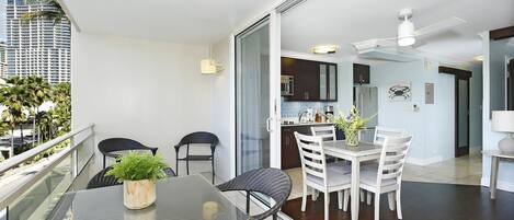 A modern apartment with a balcony, a dining area with a glass table, and a kitchen visible through an open door.