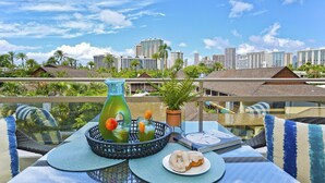 A balcony with a table set for breakfast, including a green bottle, glasses, and a plate with pastries.