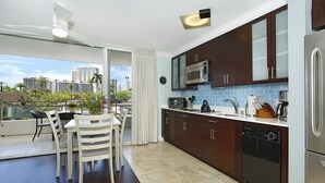 A modern kitchen with dark cabinets, a microwave, and a dishwasher. There is a dining area with a table and chairs, and a view of the city through large windows.
