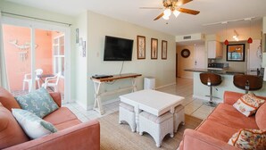 A living room with a TV, a ceiling fan, and a dining area with a bar. - Relaxing , Great Location, 3 Minute Walk To The Beach 2 Bedroom Condo by RedAwning (South Padre Island)