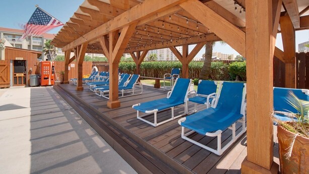A covered outdoor lounge area with wooden beams and blue lounge chairs. - Relaxing , Great Location, 3 Minute Walk To The Beach 2 Bedroom Condo by RedAwning (South Padre Island)