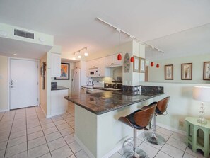 Cocina moderna con armarios blancos, encimera de granito y una isla central con taburetes de bar.