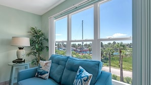 Una habitación con un sofá azul, una lámpara y un amplio ventanal con vistas a un puente y vegetación.