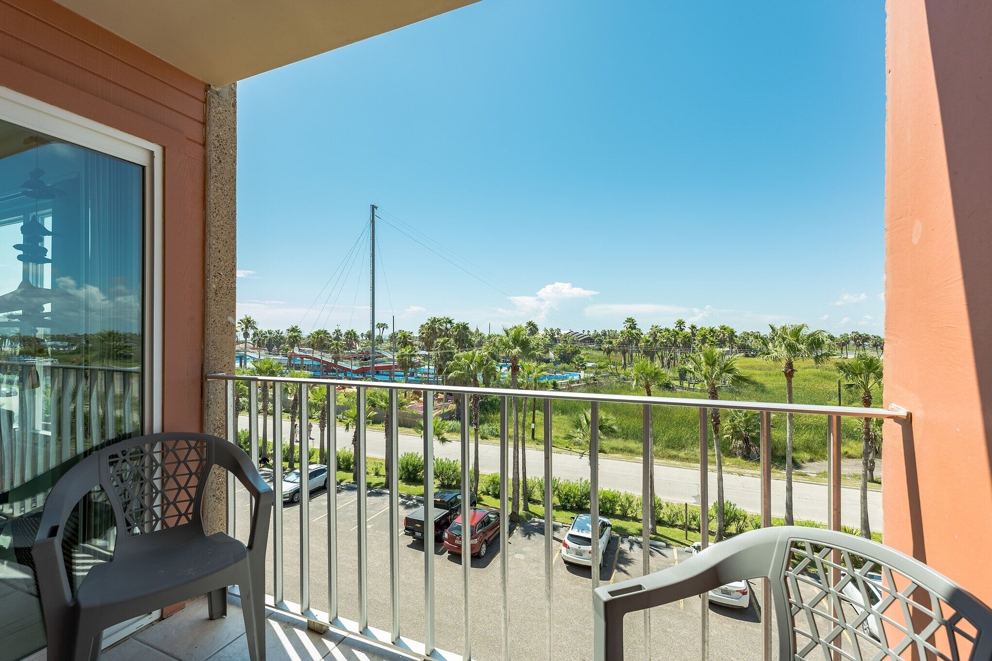 A balcony with a view of a parking lot and greenery.