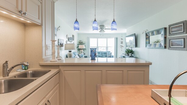 Una cocina con una isla central, pileta doble, luces colgantes y ventilador de techo.
