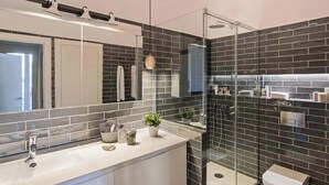 A modern bathroom with a large mirror, a glass shower enclosure, and a white vanity. - Pau Claris | Design 1BR home near Paseo de Gracia (Barcelona)