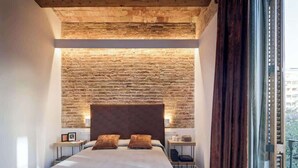 A bedroom with a large bed, a brick wall, and a view of the city. - Pau Claris | Design 1BR home near Paseo de Gracia (Barcelona)